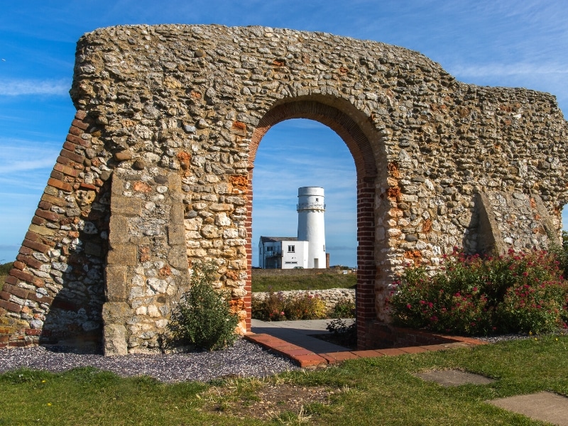 old brick wall with an arch through which can be seen a white lighthouse